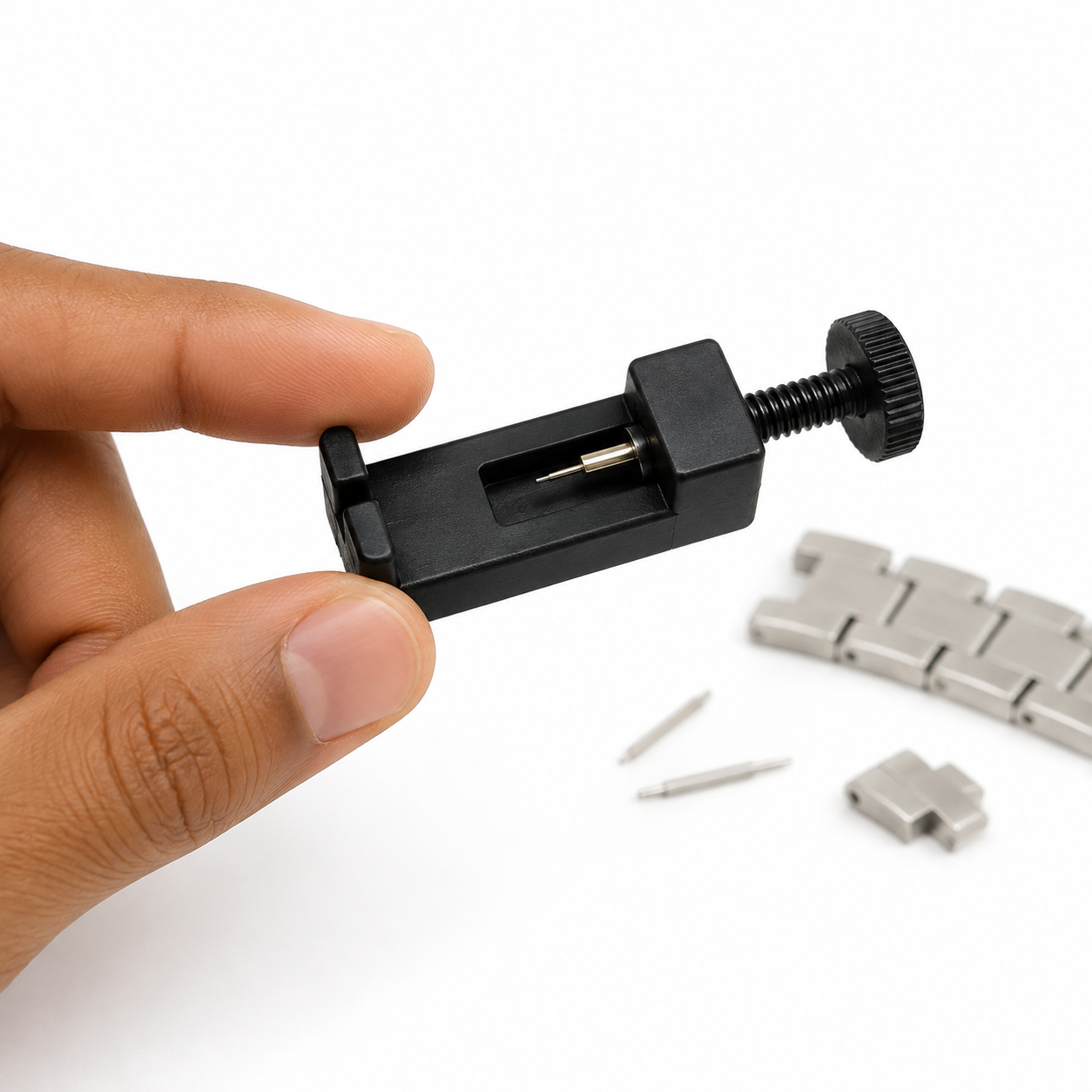 Image of Black link removal tool held beside removed steel watch links and pins