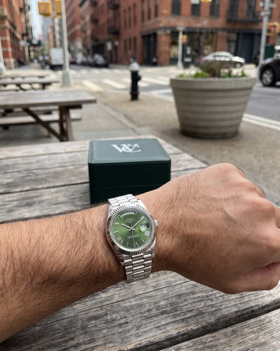 Image of William Corbier NOBLE Emerald men's green dial day-date watch, worn on a wrist beside a green gift box on a city street