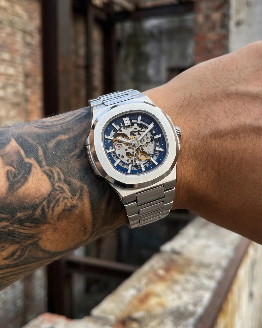 Image of William Corbier PIVOT Silver Mist men's automatic skeleton watch, worn on a tattooed forearm in an industrial setting