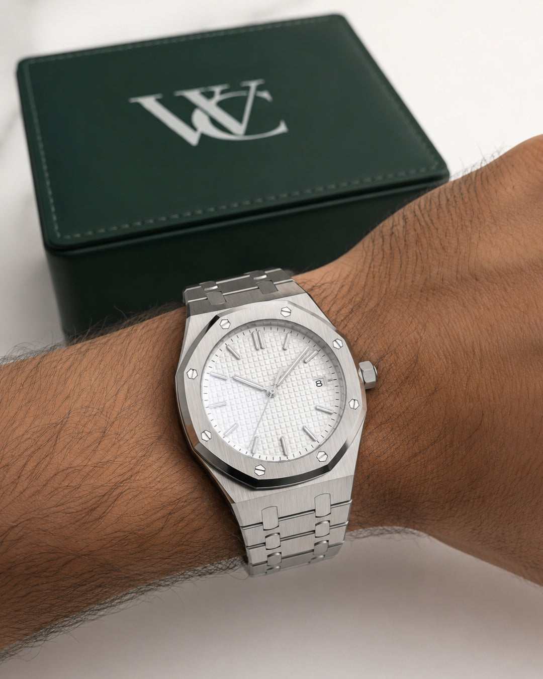 Image of William Corbier RIDGE Alpine men's white dial steel watch, worn on a wrist beside a closed green gift box